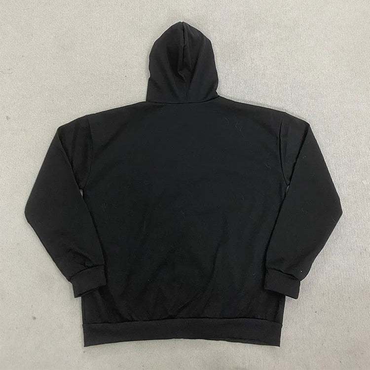A black pullover hoodie shown from the back, laid flat on a light gray concrete surface.