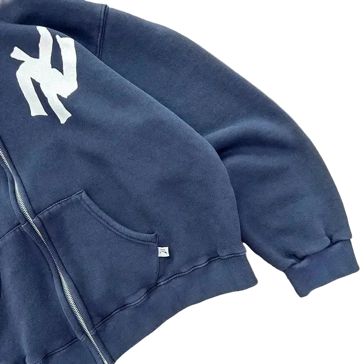 Navy blue hoodie with a logo on the chest, lying on a concrete surface.