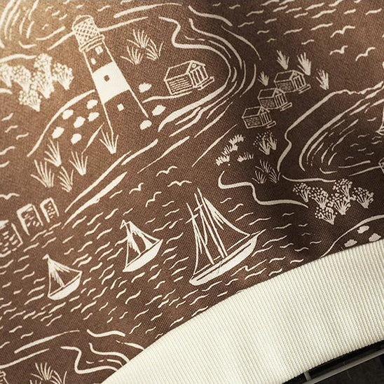 Textile with nautical pattern featuring lighthouses, ships, and houses on a brown background.