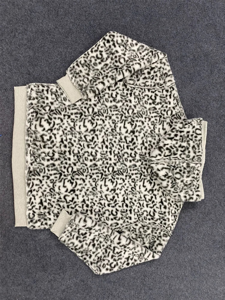 A black and white leopard print fleece jacket with beige ribbed cuffs and hem, laid flat on a dark gray textured background.