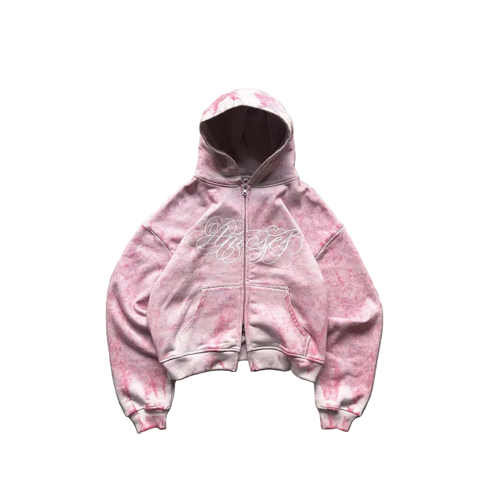Pink tie-dye hoodie with text on a concrete surface with greenery