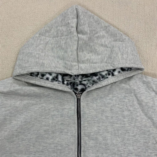 A light gray heather zip-up hoodie laid flat on a beige textured fabric background, featuring a black and gray leopard-print lining inside the hood.